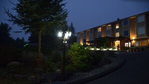 Un bâtiment à l’architecture moderne, doté d’un espace extérieur couvert avec des sièges et d’un jardin bien entretenu, agrémenté d’arbres et d’arbustes.