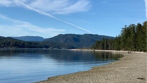 Un lac paisible, avec une plage de galets et des montagnes boisées en arrière-plan.