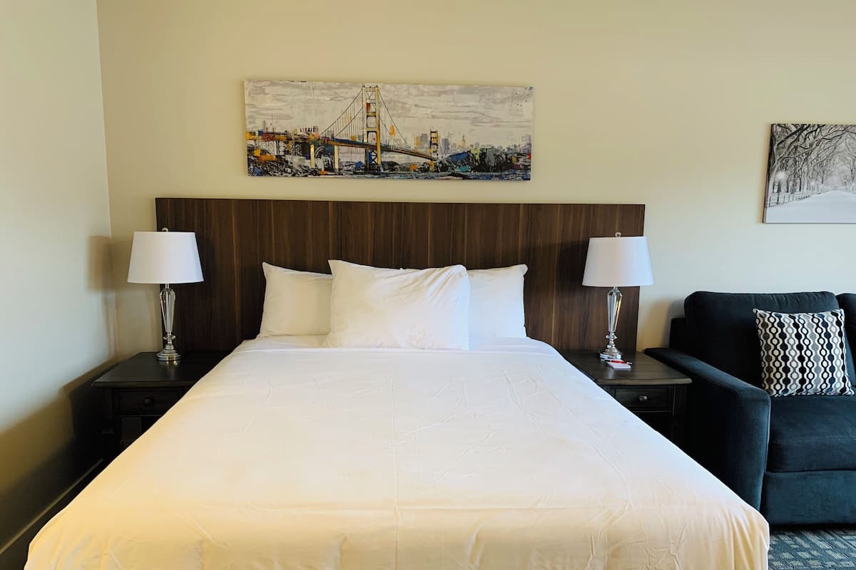 Une chambre d’hôtel avec un grand lit, deux tables de chevet avec des lampes, une tête de lit sombre et deux tableaux accrochés aux murs.