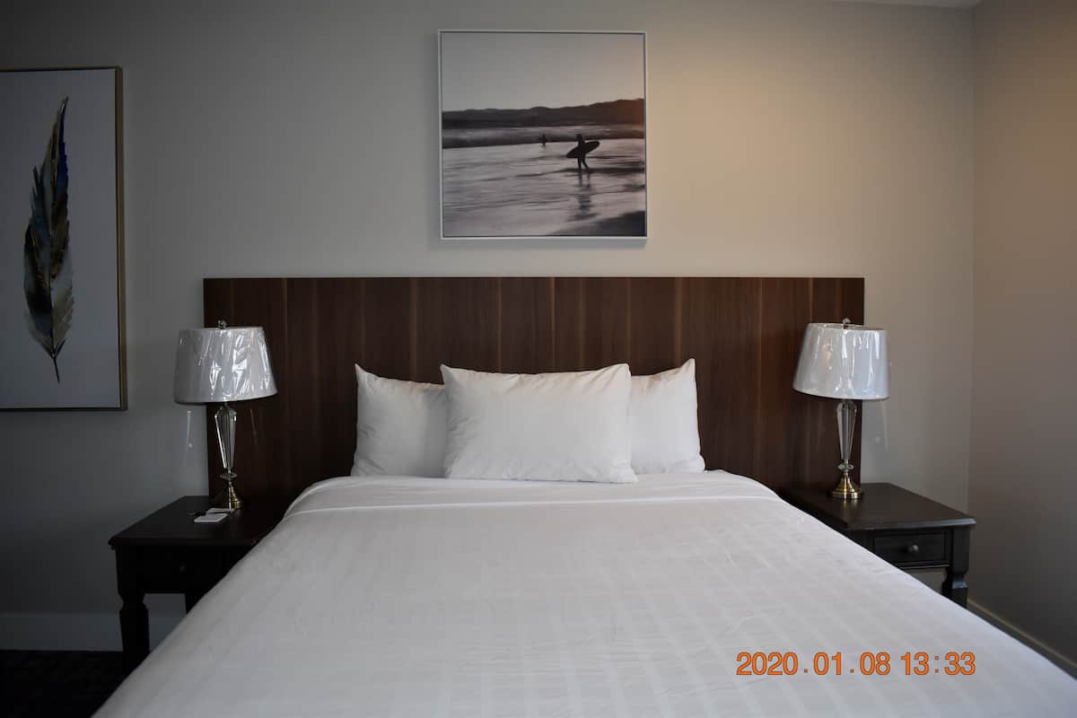 Une chambre d’hôtel avec un grand lit, deux tables de chevet avec des lampes, un tableau encadré au mur et une tête de lit en bois.