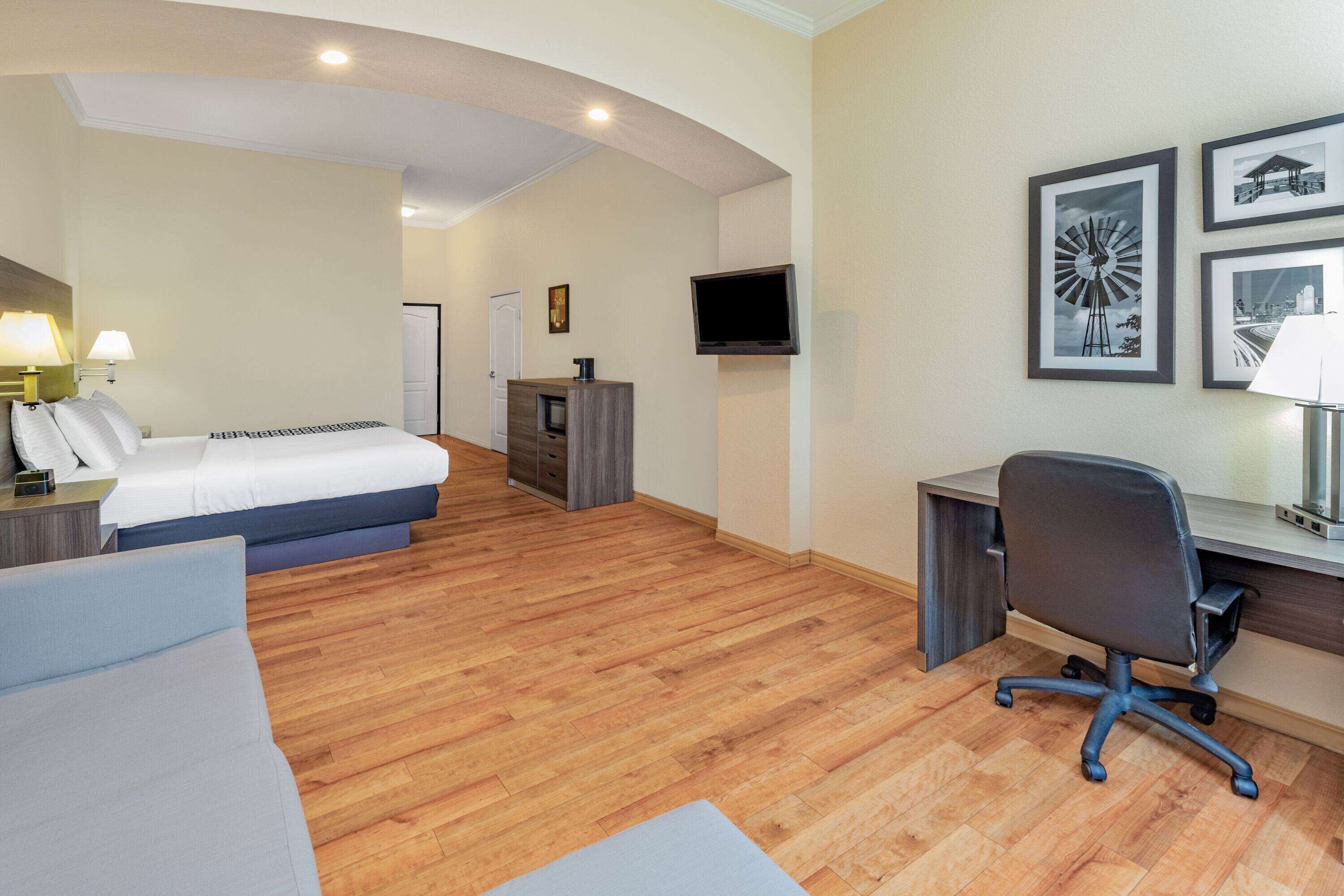 Habitación de hotel con cama, escritorio, silla, televisión y cuadros en la pared.