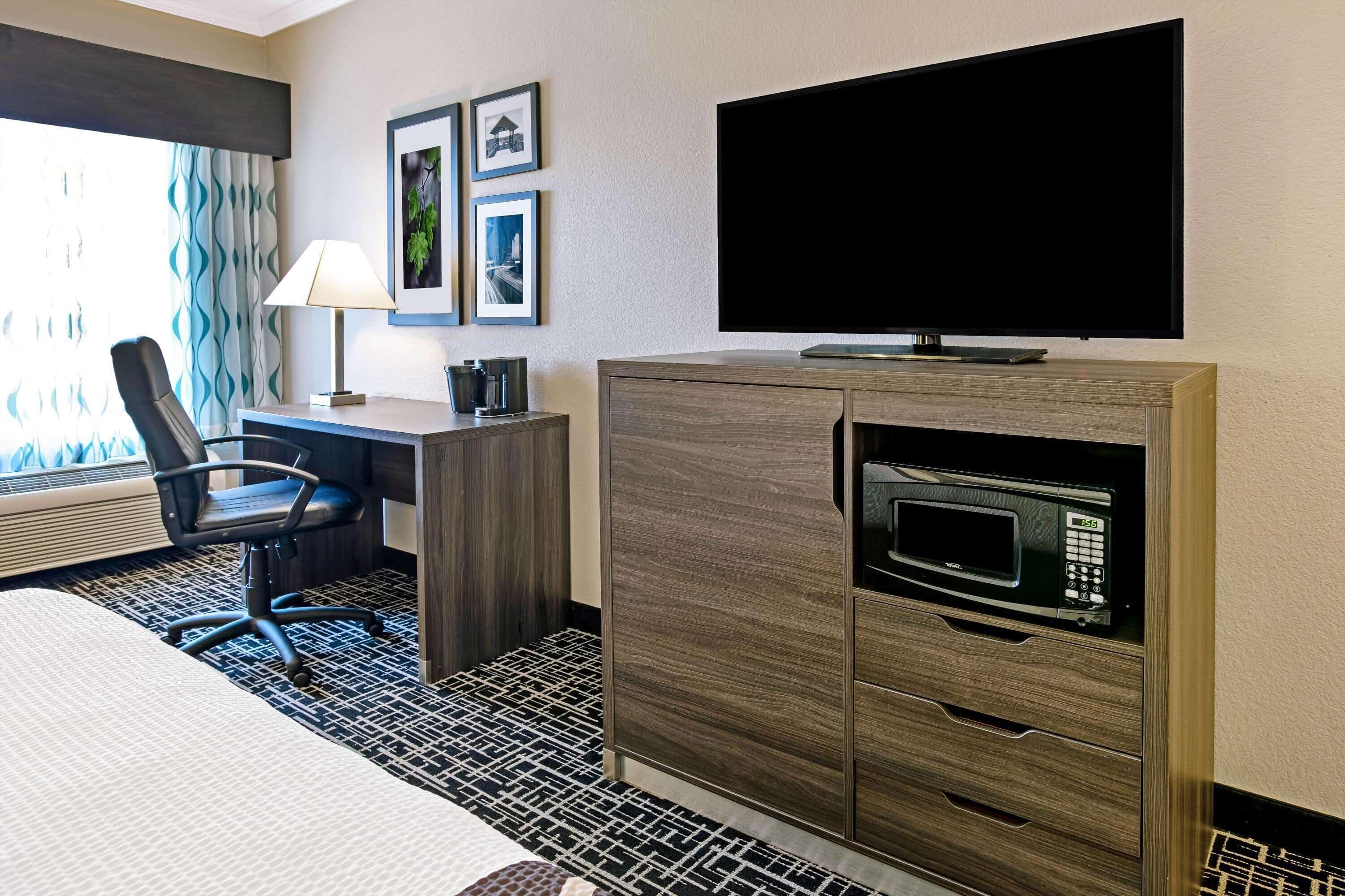 A hotel room with a bed, a desk, a chair, a TV, a microwave, and a window with curtains.