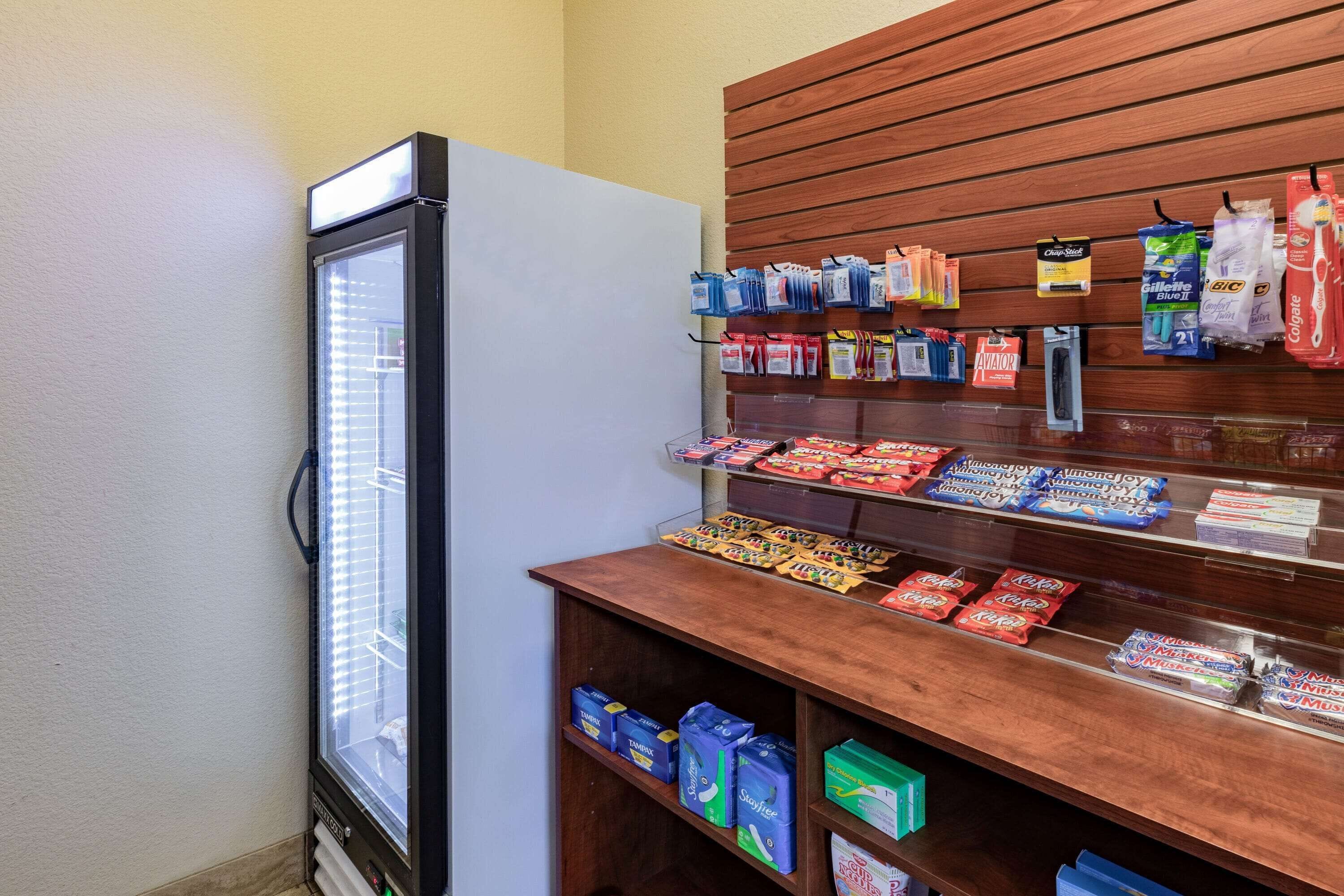 A refrigerated display case with various packaged goods, a wooden counter with snacks, and a wall-mounted display of toiletries.