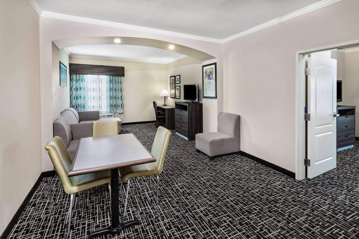 Een hotelkamer met een eethoek, een bank, een televisie en een deur naar een andere kamer.