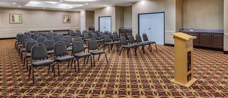 A conference room with rows of chairs, a podium, and a patterned carpet.