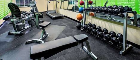 Un gimnasio con cintas de correr, una banca y un estante con mancuernas.