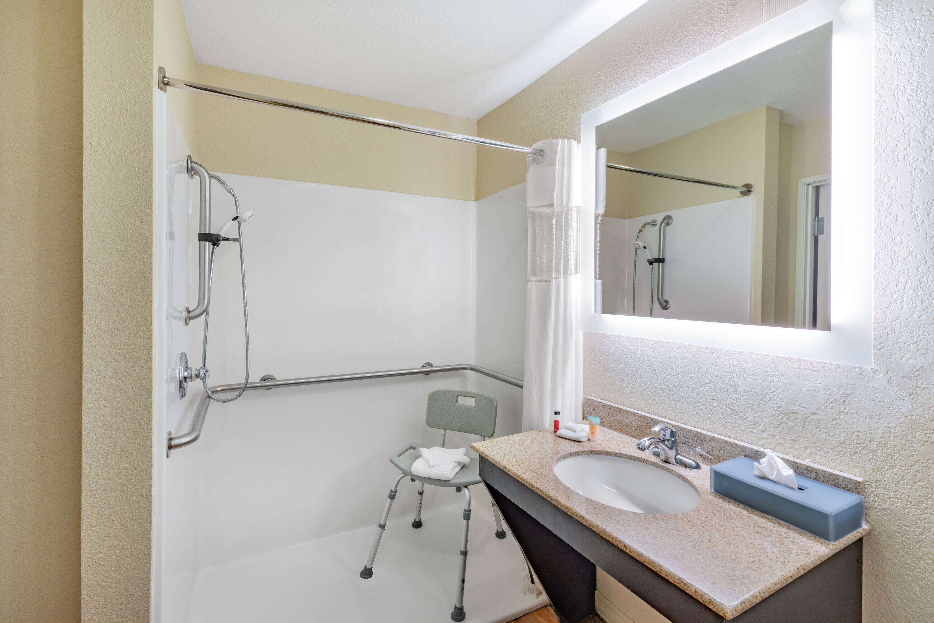 A bathroom with a shower, grab bar, and a sink with a mirror.