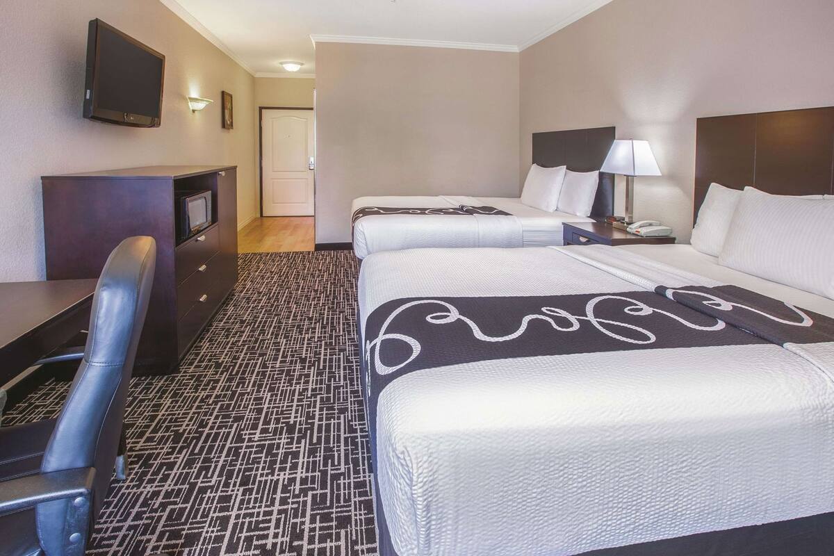 Una habitación de hotel con dos camas, un escritorio, una silla, un televisor y una lámpara.
