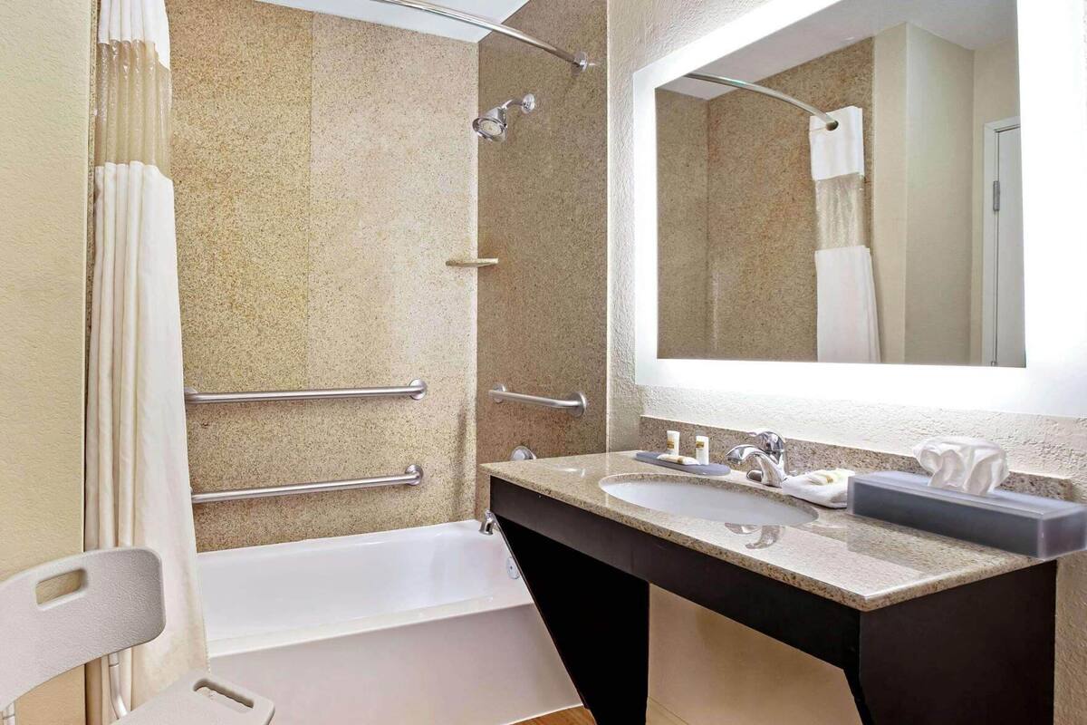 Un baño con bañera, lavamanos con espejo y barras de apoyo.