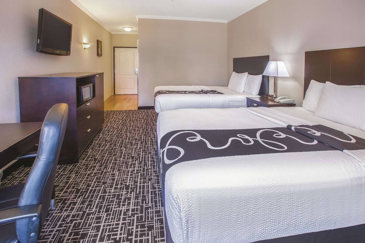 Een hotelkamer met twee bedden, een bureau, een stoel, een televisie en een lamp.