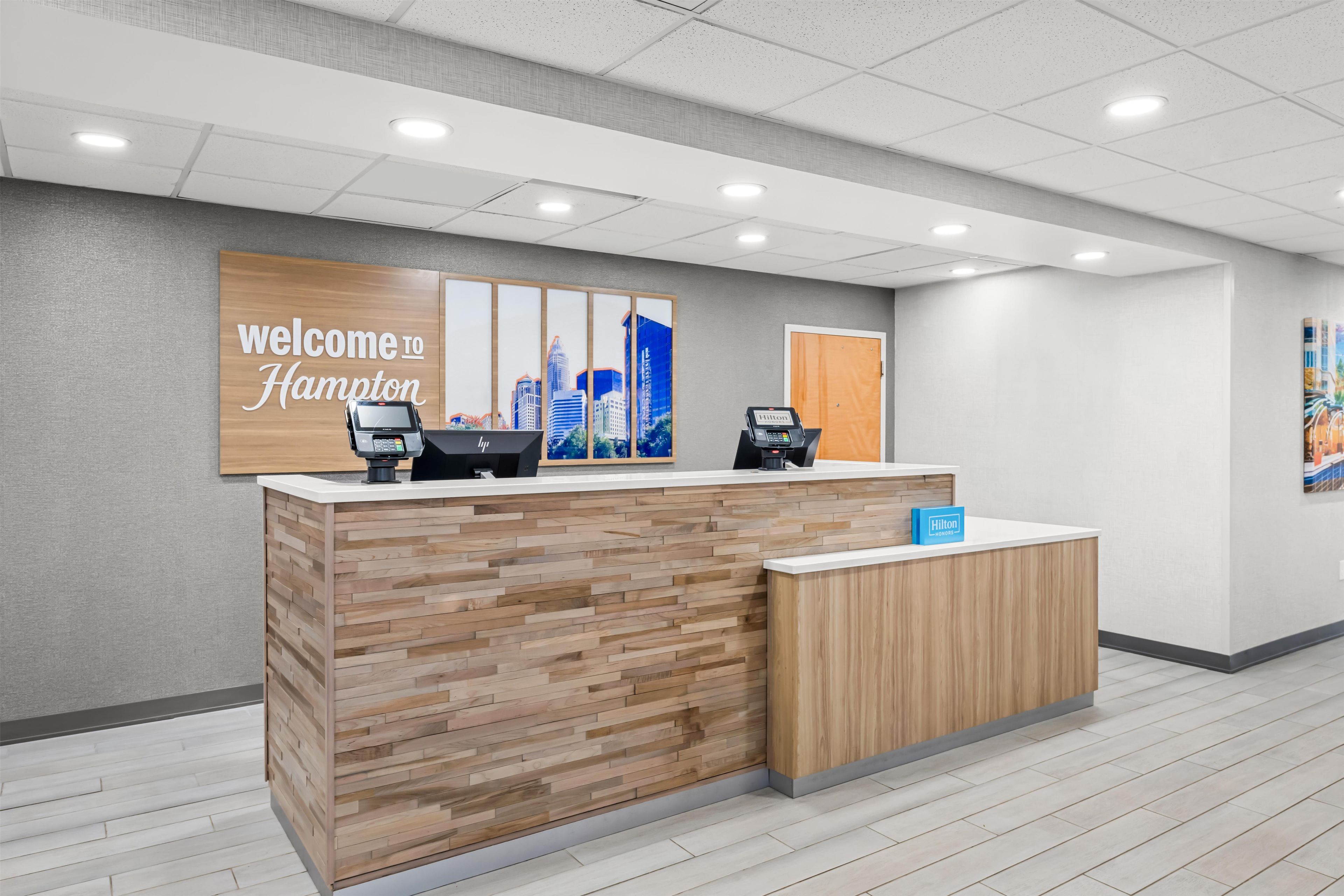A reception desk with a cityscape mural, two card readers, and a 'Welcome to Hampton' sign.