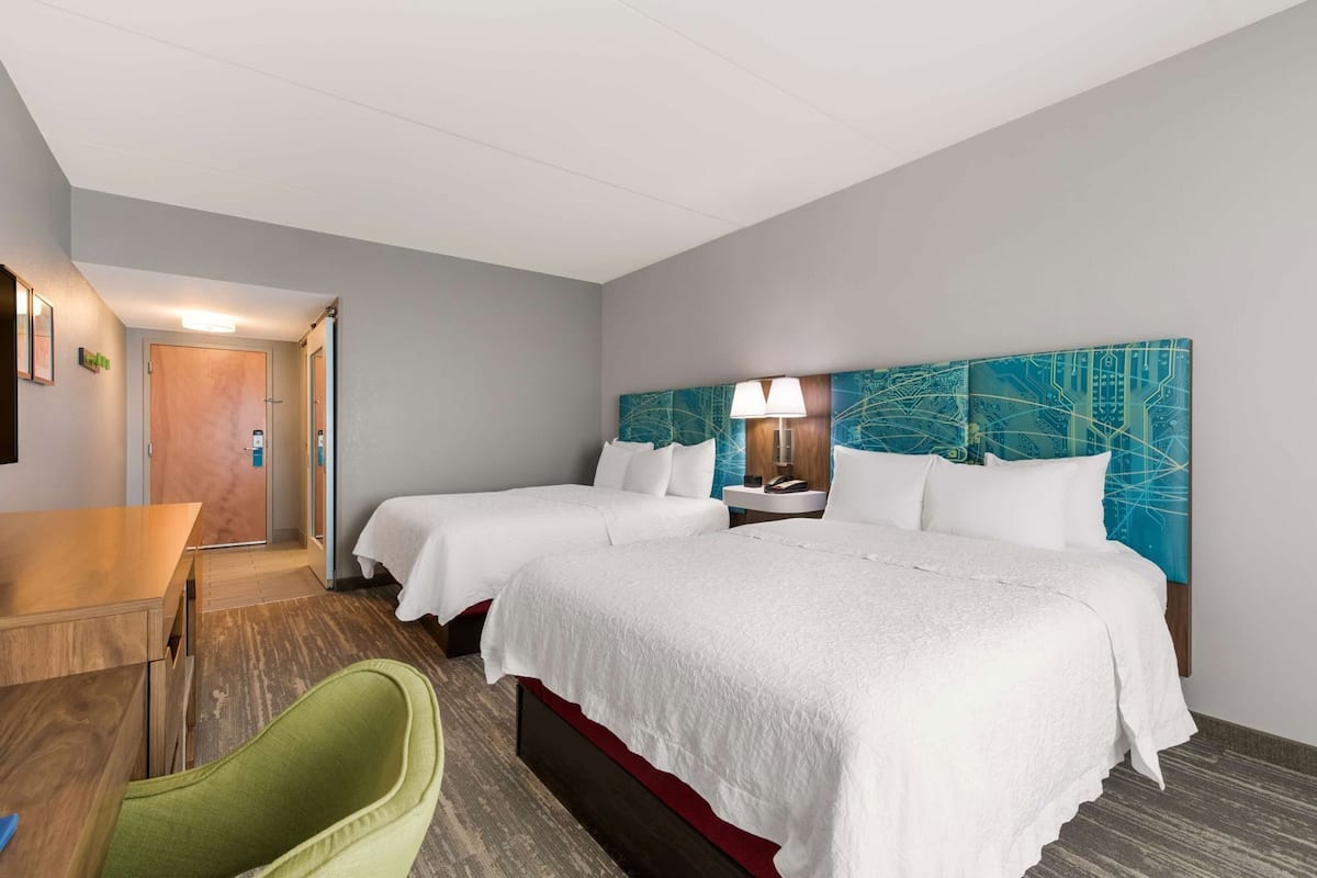 A hotel room with two beds, a desk, a chair, and a bathroom door.