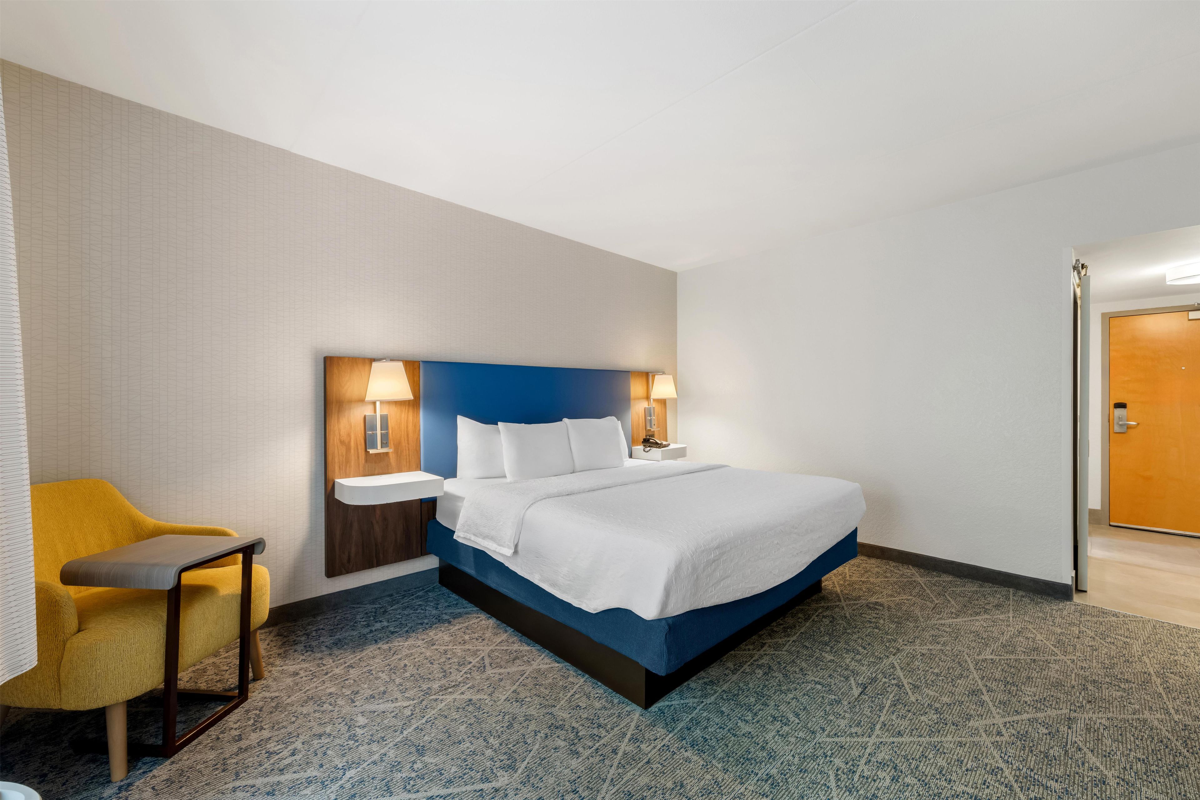 A hotel room with a bed, bedside tables, a chair, and a door.