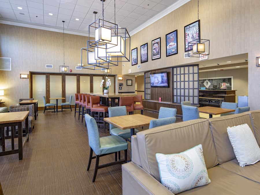 Een ruim restaurant met verschillende zithoeken, waaronder zitbanken en tafels, en een televisiescherm aan de muur.
