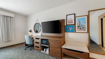 A hotel room with a flat-screen TV, a desk with a chair, a mirror, and framed pictures on the wall.