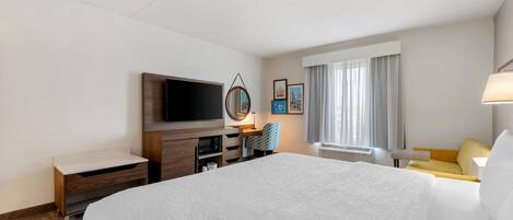 Una habitación de hotel con una cama grande, un televisor de pantalla plana, un escritorio con una silla, una ventana con cortinas y un espejo montado en la pared.