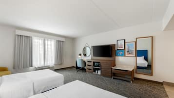 A hotel room with two beds, a TV, a desk with a chair, a mirror, and artwork on the wall.