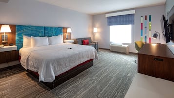 Una habitación de hotel moderna con una cama grande, dos mesitas de noche con lámparas, un escritorio, una silla y una ventana con persianas.