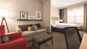 Een hotelkamer met een bed, een slaapbank, een rode fauteuil, een kleine tafel en kunst aan de muur.