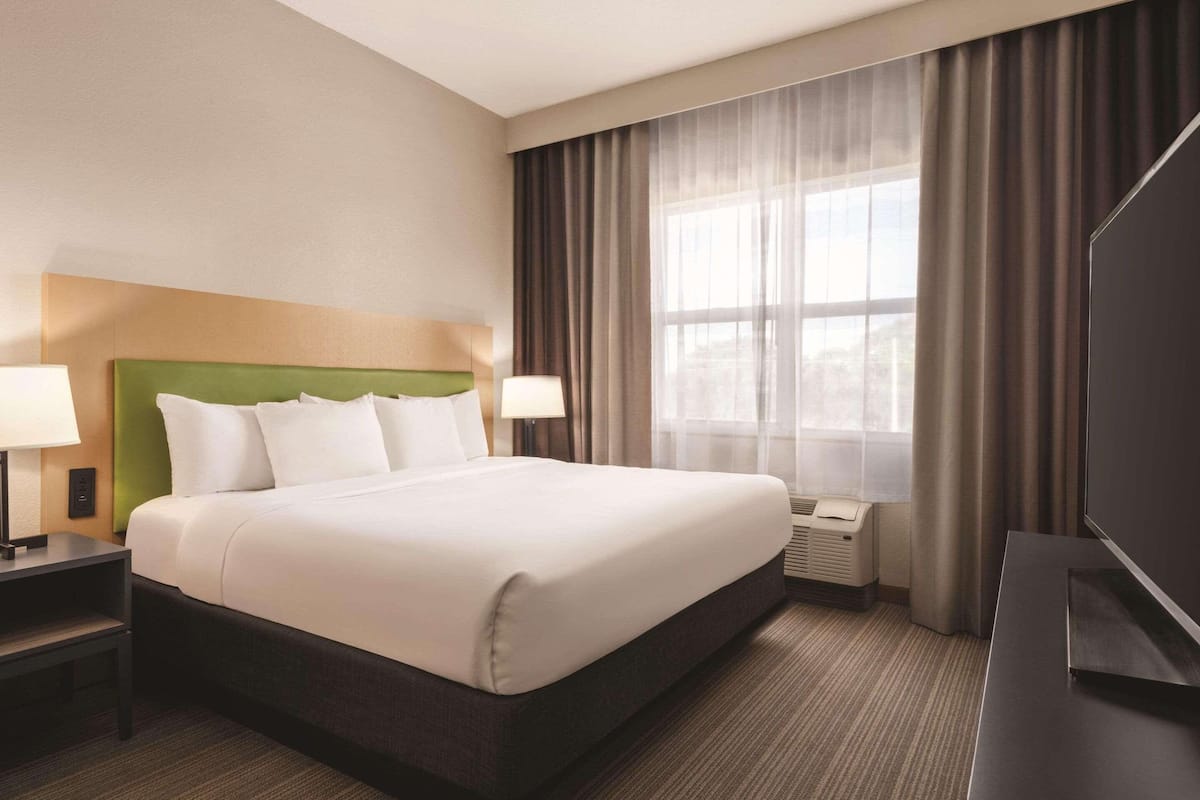 A hotel room with a large bed, two bedside tables, a flat-screen TV, and a window with curtains.