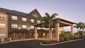 Een Country Inn & Suites hotel met een overdekt buitenzitgedeelte, palmbomen en een goed verlichte ingang.