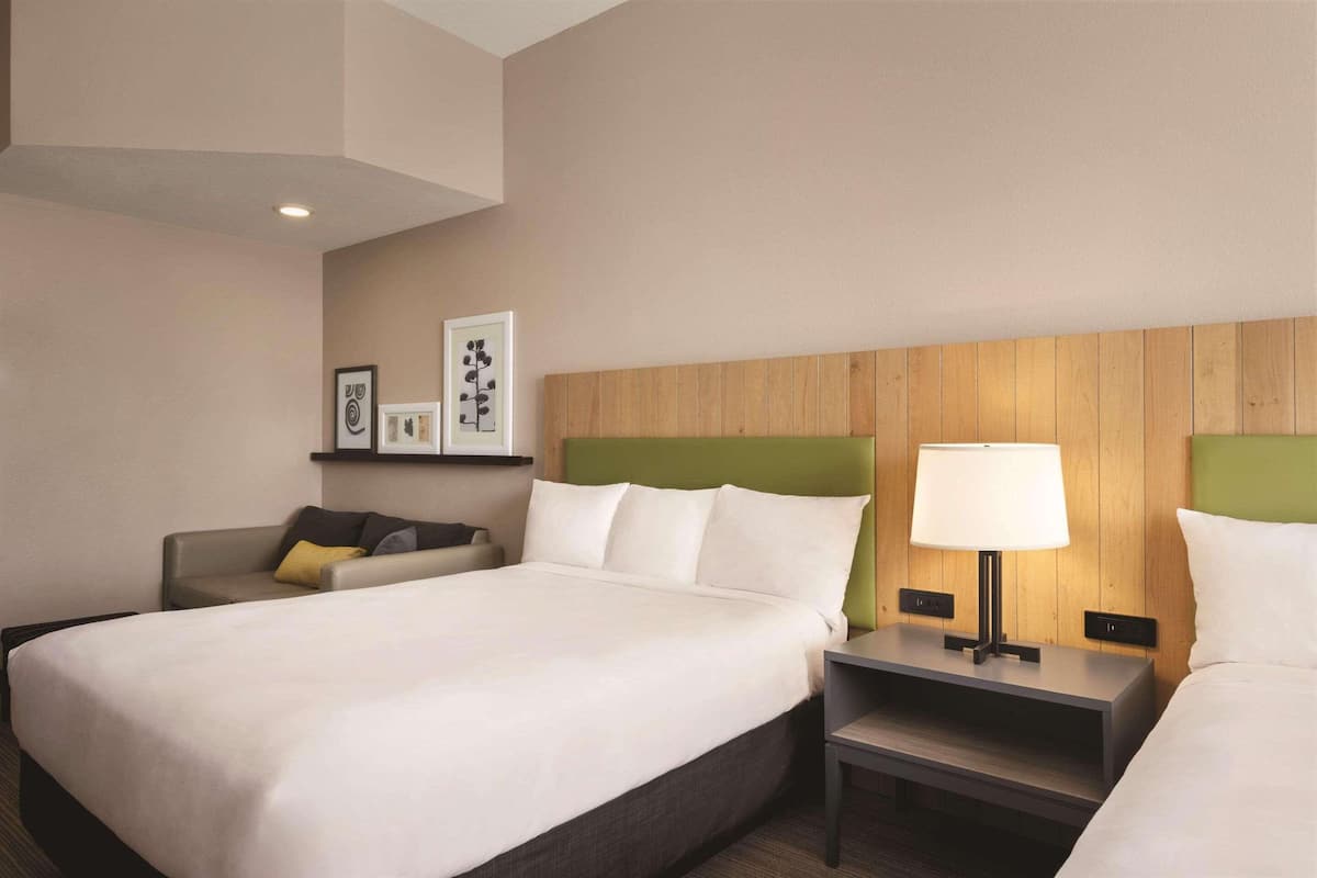 A hotel room with a large bed, a bedside table with a lamp, a small sofa, and a wooden headboard.