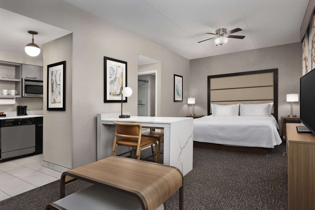 A hotel room with a bed, desk, chair, and kitchenette.