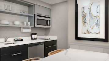 A modern kitchen with a built-in microwave, a coffee maker, and a sink. There is a dining table with chairs and a framed artwork on the wall.