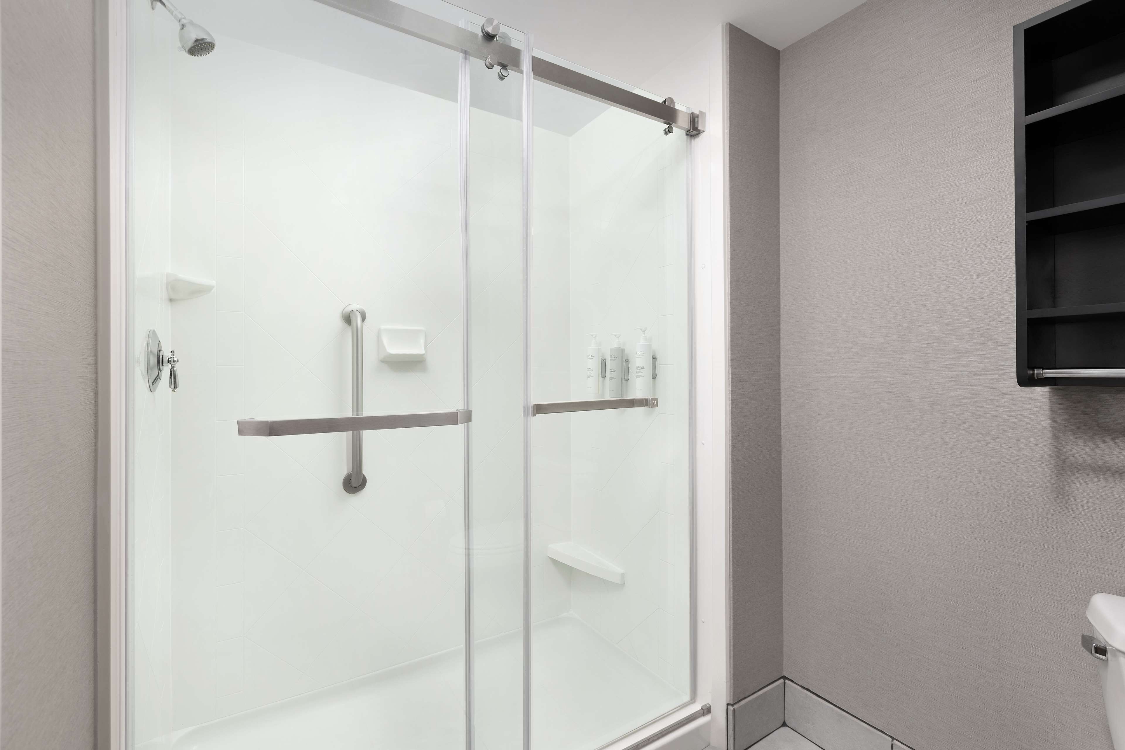 A modern bathroom with a glass-enclosed shower, a toilet, and a shelf with toiletries.