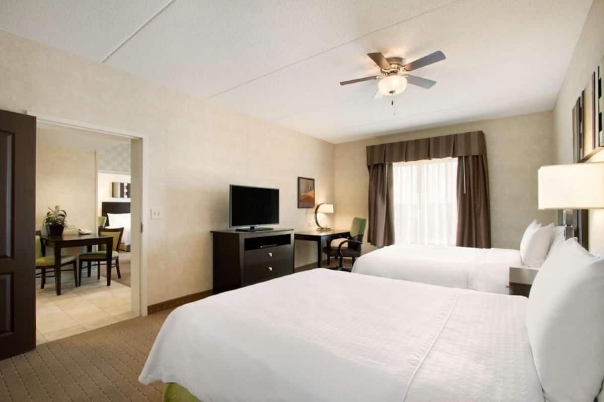 A hotel room with two beds, a television, a desk, and a dining area.