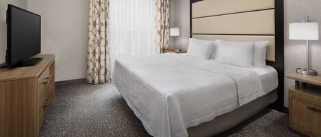 Una habitación de hotel con una cama grande, un televisor sobre un mueble de madera y un ventilador de techo.