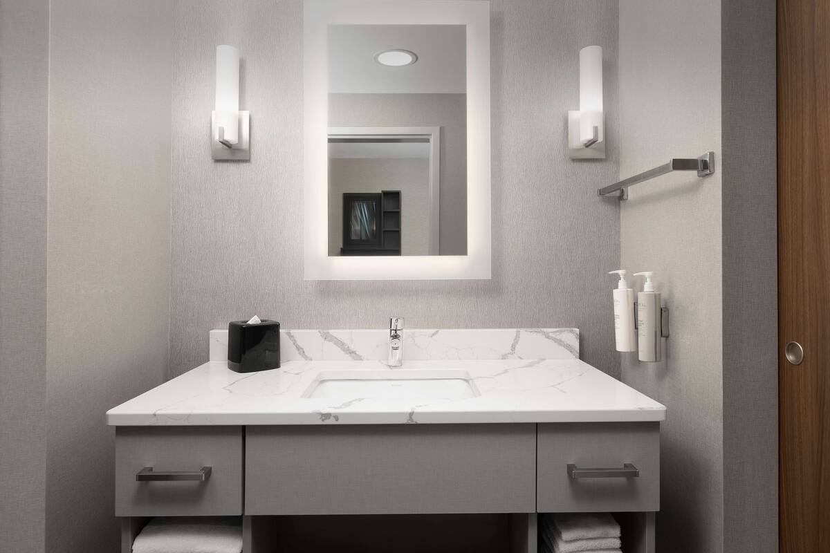 A modern bathroom with a marble sink, two towel racks, and a mirror with wall sconces.