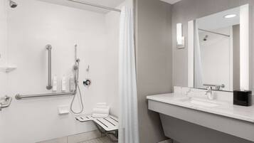 Un baño moderno con cabina de ducha, barras de apoyo, tocador con espejo y perchero para toallas.