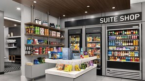 A modern hotel suite shop with shelves stocked with snacks, beverages, and toiletries.