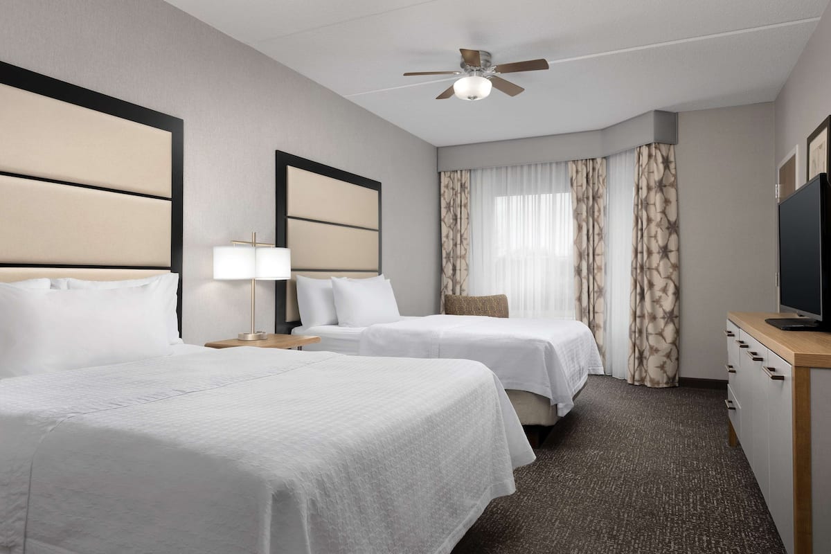 A hotel room with two beds, a ceiling fan, a TV, and a desk.