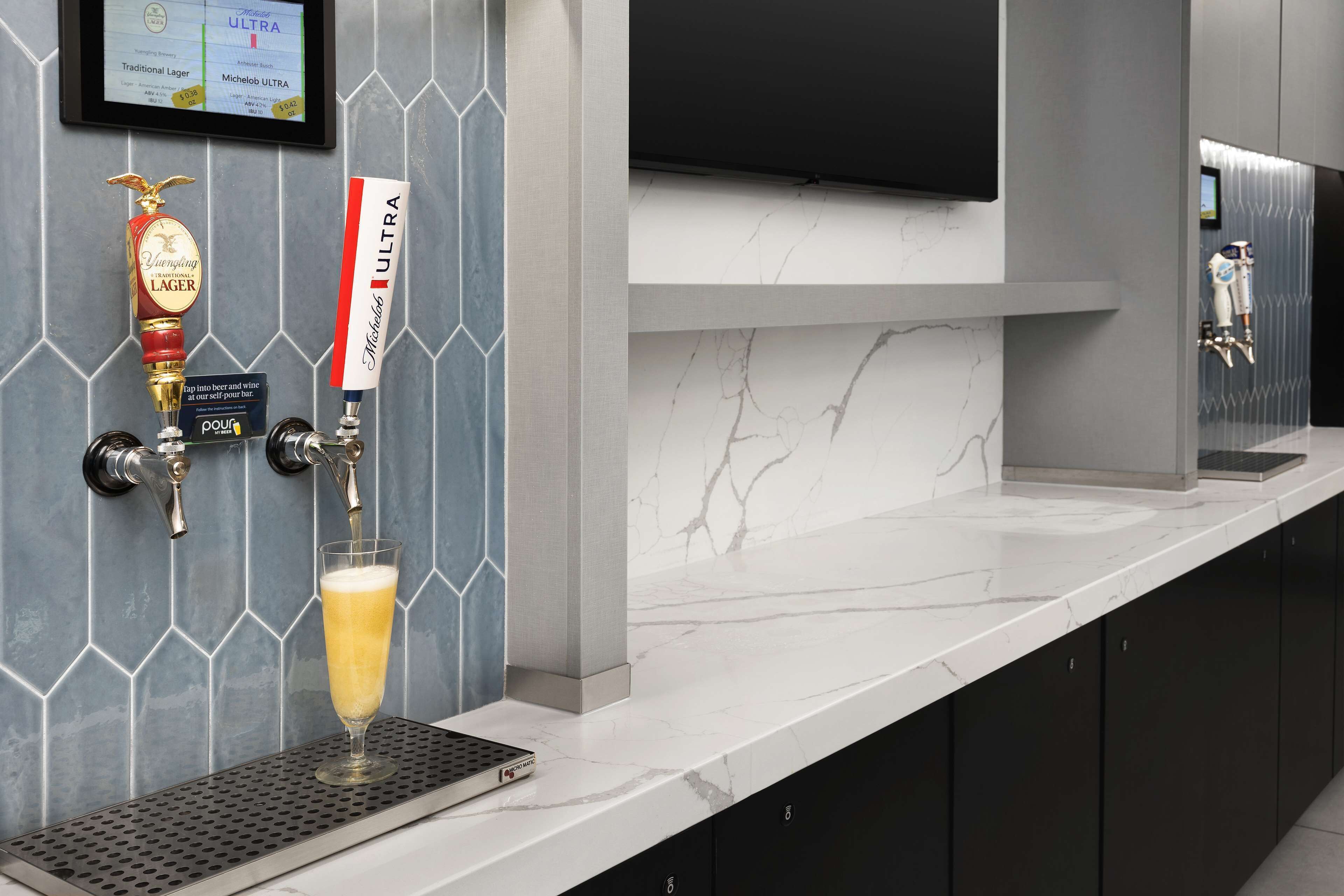 Zona de bar moderna con una grifo sirviendo cerveza, una jarra de cerveza en una bandeja y un televisor montado.