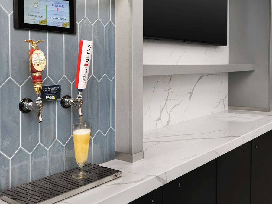 Zona de bar moderna con una grifo sirviendo cerveza, una jarra de cerveza en una bandeja y un televisor montado.