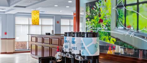 A coffee station with multiple dispensers, a reception desk, and a large window with a garden view.