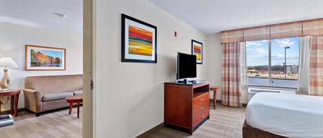 Habitación de hotel con cama, escritorio, sillón, televisión y cuadros en la pared.