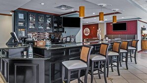 Eine Bar mit einer Theke, Barhocker und einem an der Wand befestigten Fernseher.