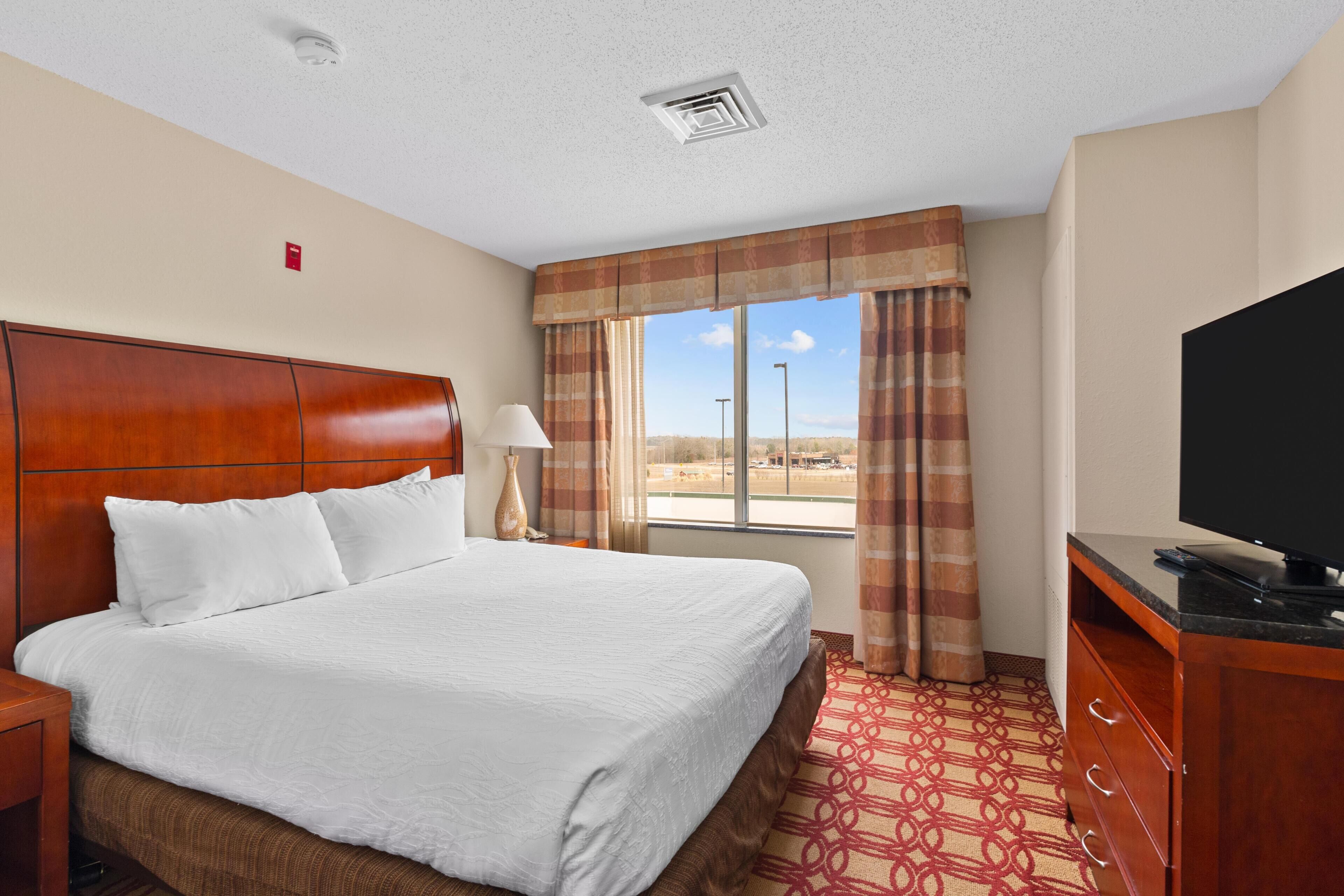 A hotel room with a bed, a television, a desk, and a window with curtains.