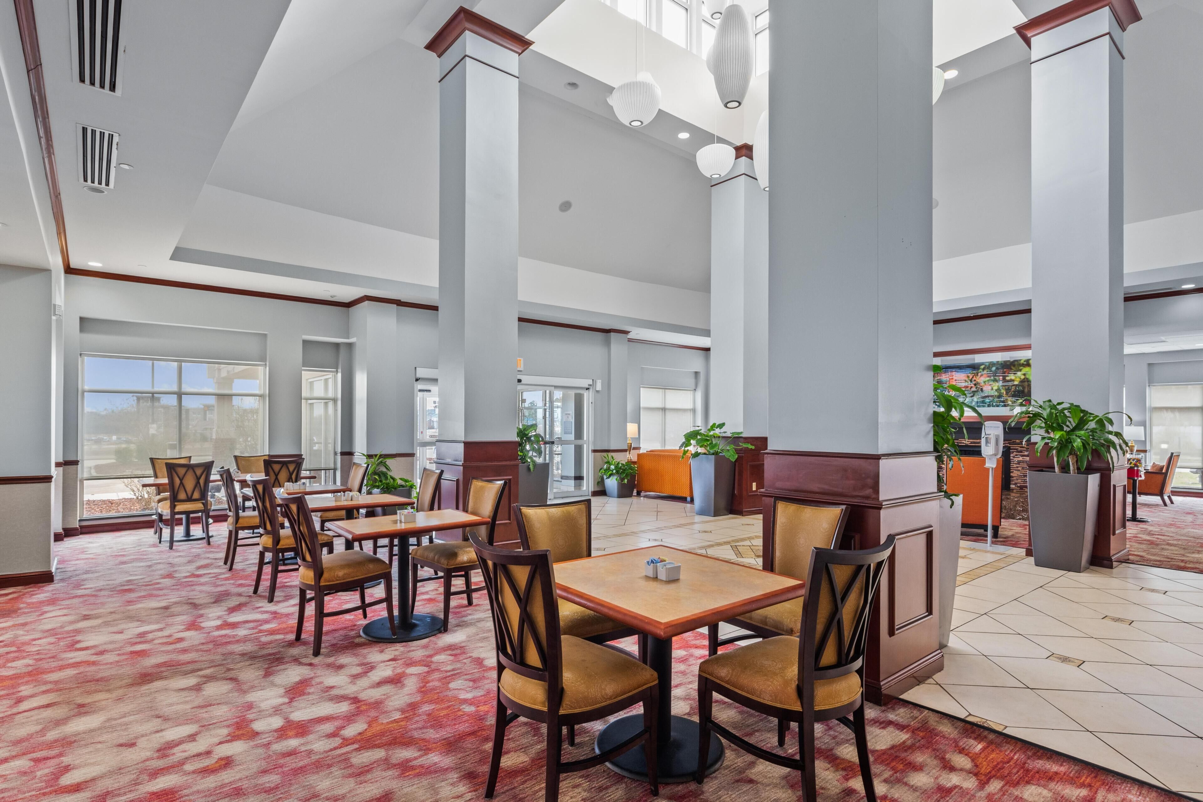A spacious lobby with high ceilings, large windows, and a red patterned carpet.