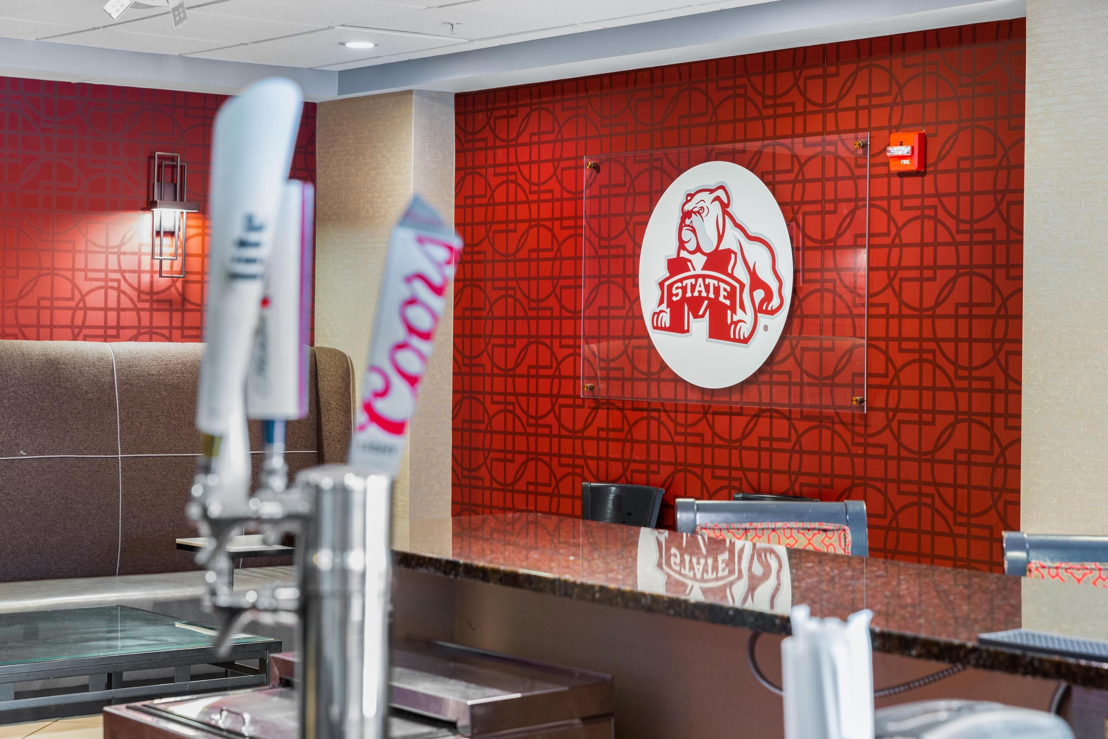 Een restaurantinterieur met een rode, geruite wand, een logo met een buldog en een toonbank met een koffieapparaat.