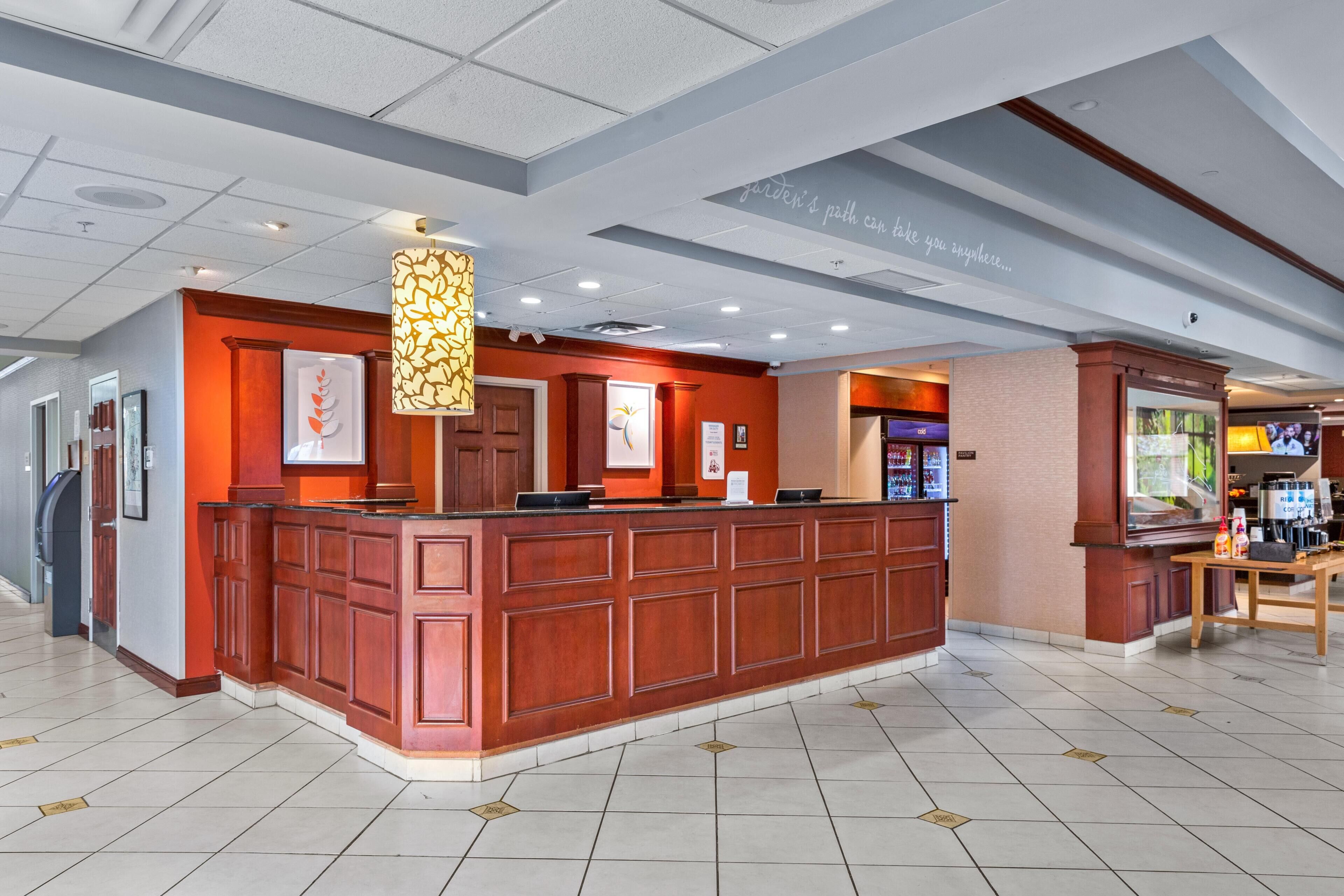 A hotel reception area with a wooden reception desk, a large wall-mounted sign, and a ceiling with recessed lighting.