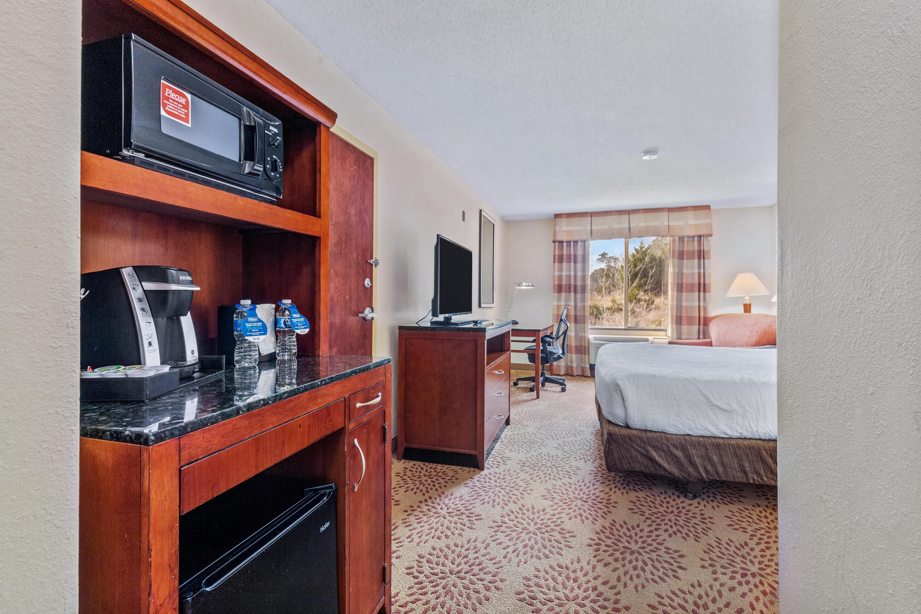 A hotel room with a bed, a desk with a computer, a microwave, and a coffee maker.