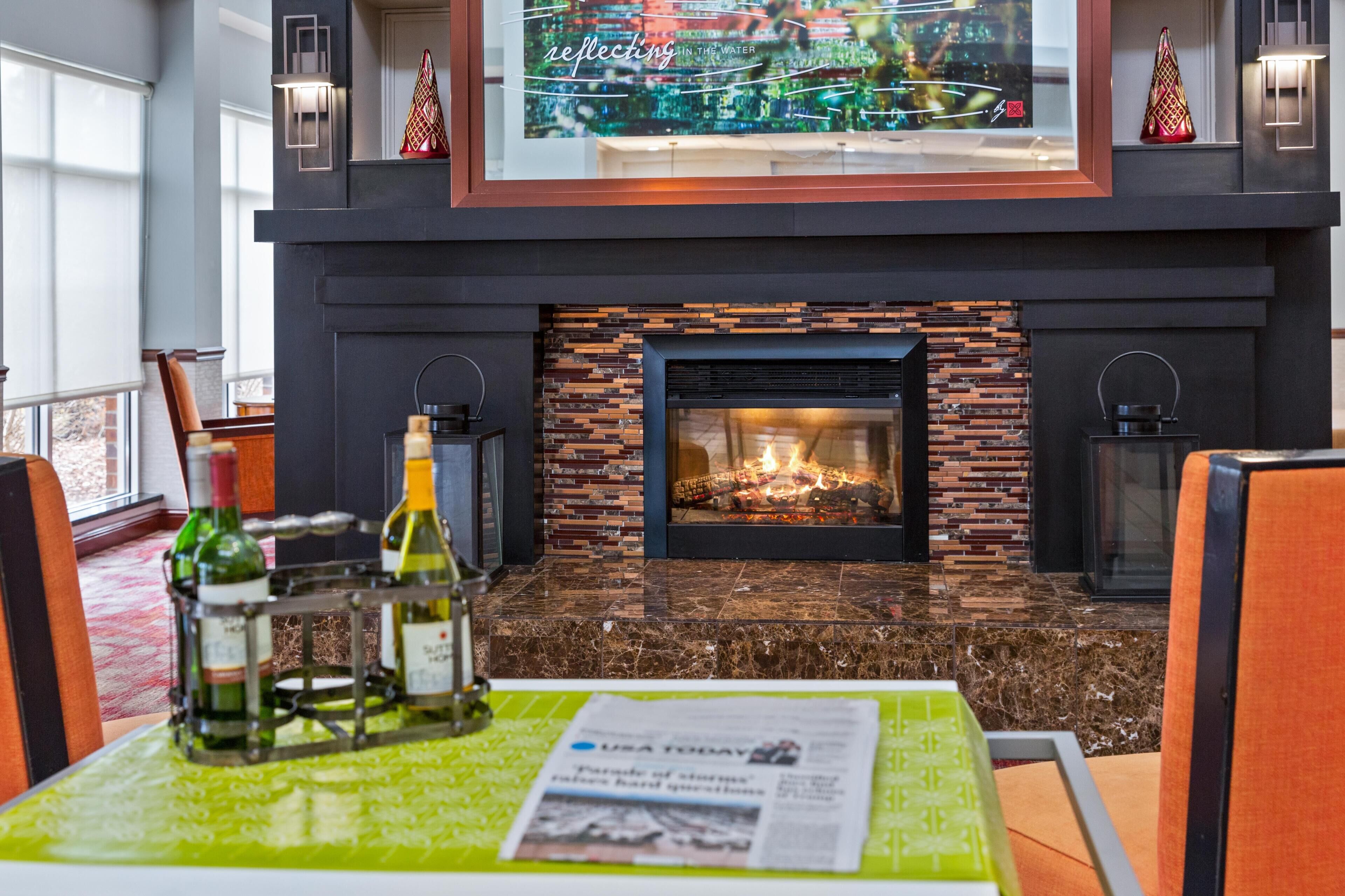 A dining area with a fireplace, a table with a newspaper, and a window with a cityscape view.