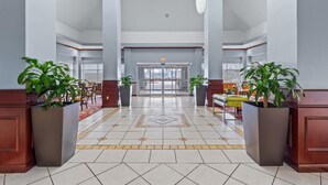 Eine geräumige Lobby mit Fliesenboden, großen Kübelpflanzen und einer Glastür.