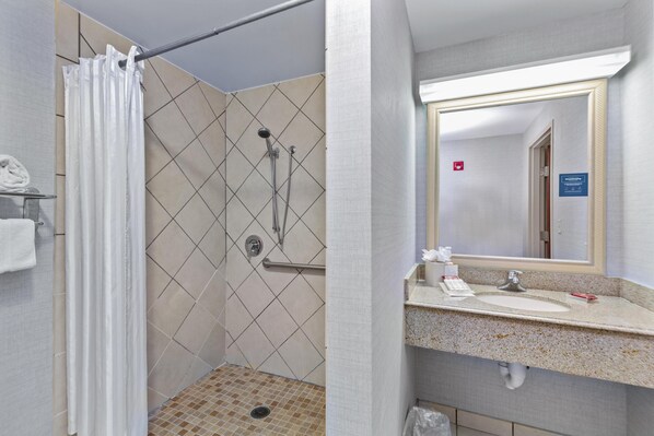 Un baño con ducha, lavamanos, espejo y toallero.