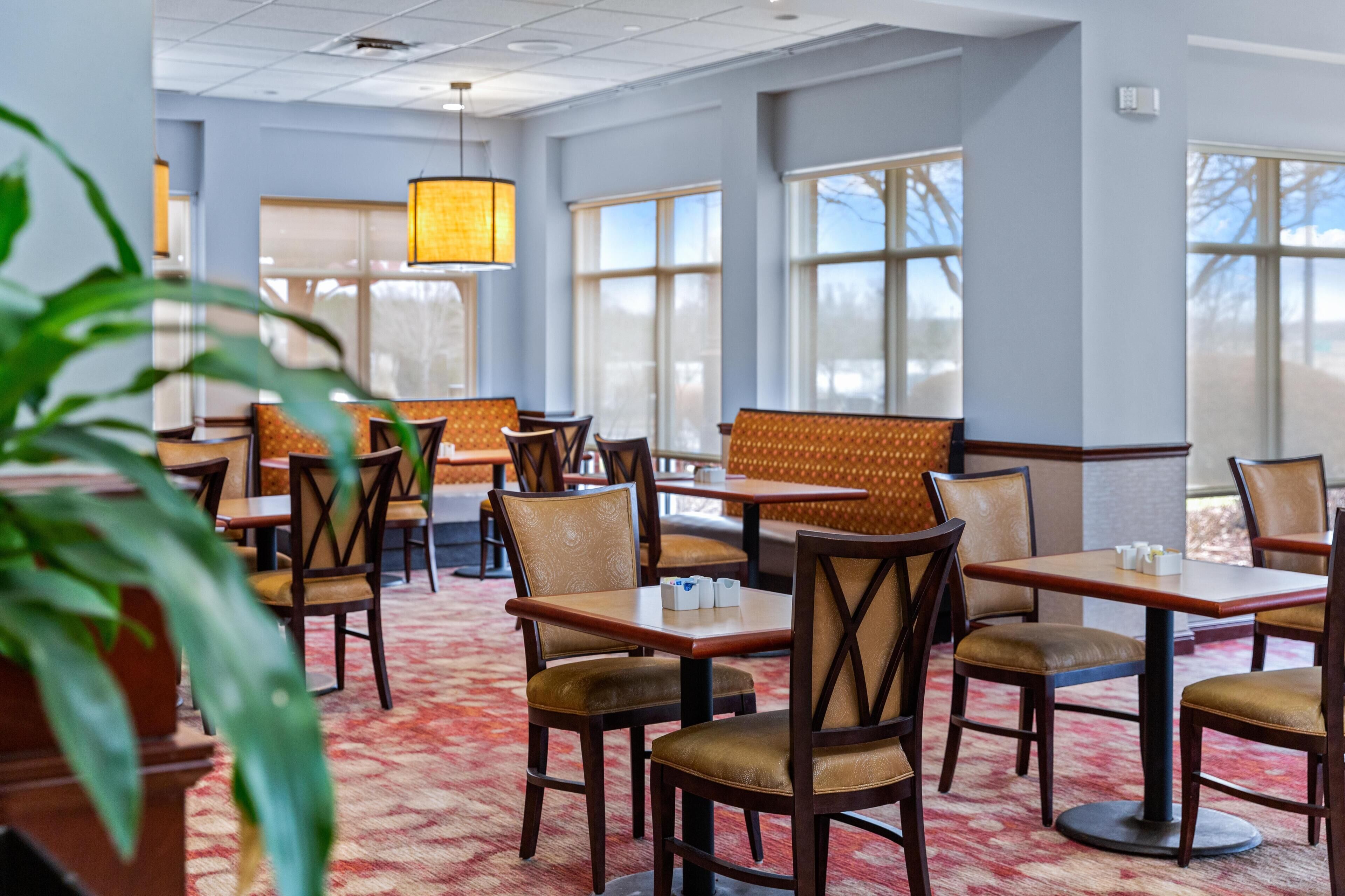 Ein Hotel-Speisesaal mit Tischen, Stühlen, großen Fenstern und einem gemusterten Teppich.
