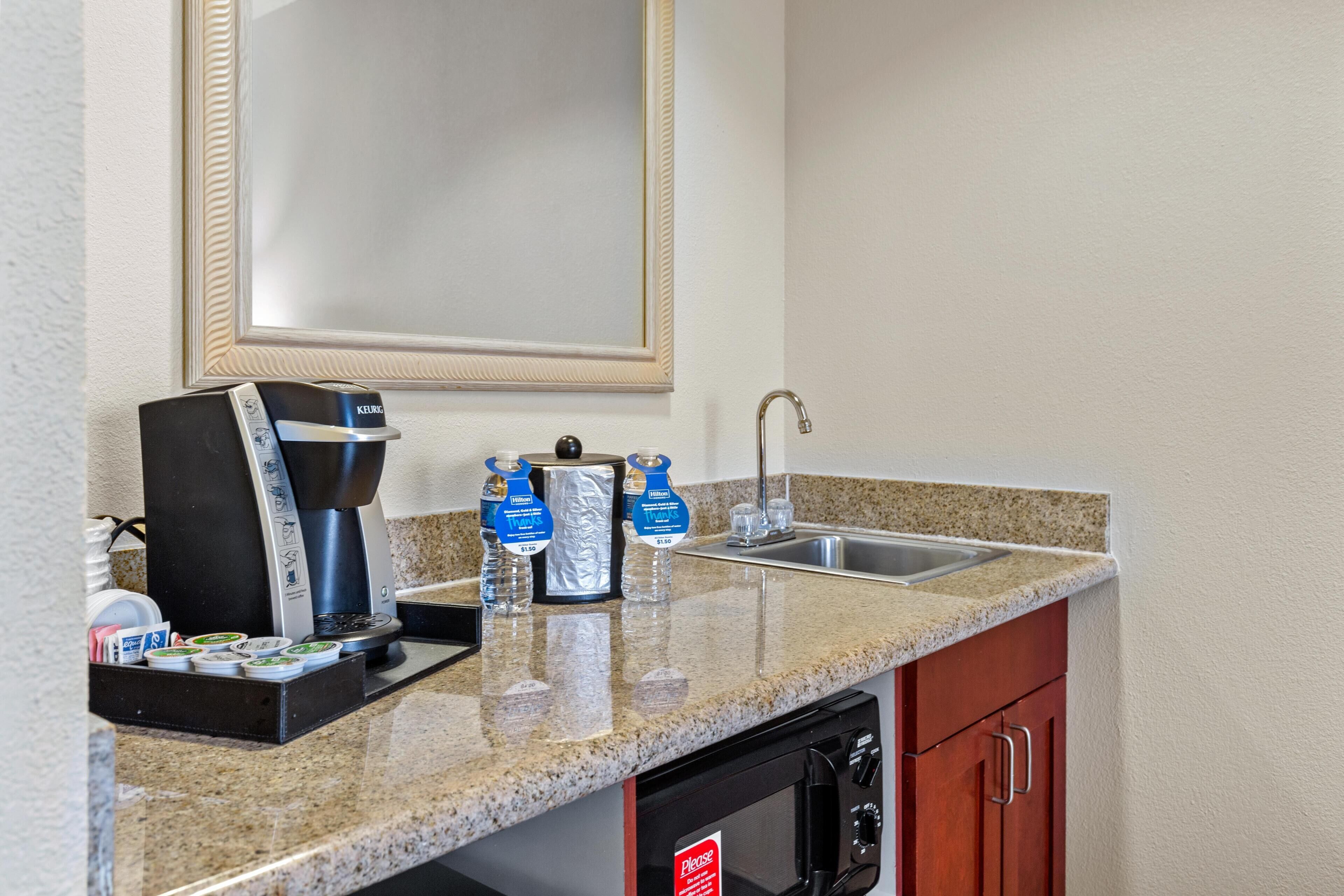 A kitchenette with a coffee maker, water bottles, a sink, and a dish soap dispenser.